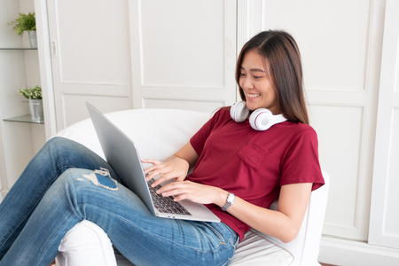 Asian woman with headphone using laptop computer with relax pose at couch in living room at home.leisure lifestyleの写真素材