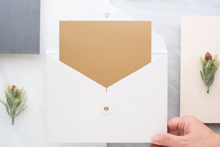 Top view of hand holding blank gold card in white envelop with pine leaf on two layer step of marble...