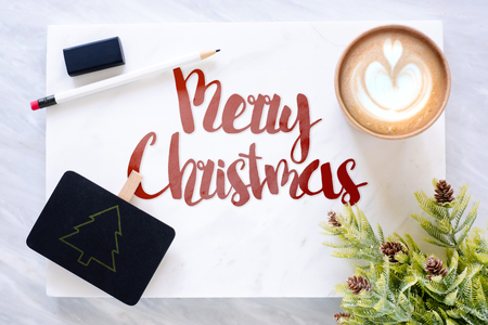 Top view of red merry christmas text on marble table with blackboard, pencil, eraser pine leaf and coffee cup.holiday greeting cardの写真素材