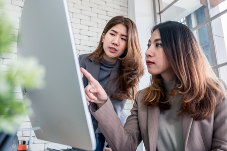 Two colleague businesswoman discussion about work use desktop computer at window in modern office.Digital business lifestyle conceptの写真素材
