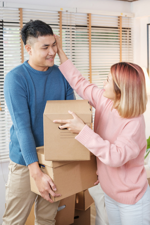 Happy asian couple carry cardboard boxes while moving to new house in living room.unpacking for new home.woman wipe the sweat her husbandの写真素材