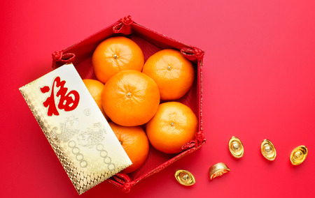 Group of orange tangerine in Chinese pattern tray and envelope packet ang pow with gold ingots on red table top. Chinese new year concep.Chinese Language on envelop is happiness,on ingot is wealthyの写真素材