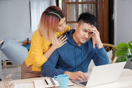 Asian female girlfriend encouragement boyfriend from stress while working on home budget on laptop at living room in home