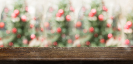 Empty rustic wood table top with abstract blur christmas tree red decor ball and snow fall background with bokeh light,winter Holiday backdrop,Mock up banner for display of product or promotionの写真素材
