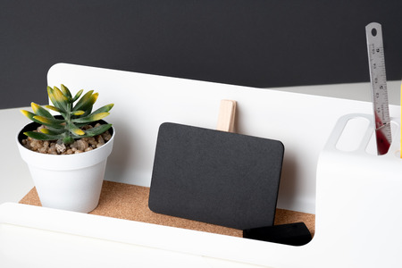Black clip blackboard on modern pencil box and green plant in white pot on table and dark grey wall in office desk,mock up space for display of design or textの写真素材