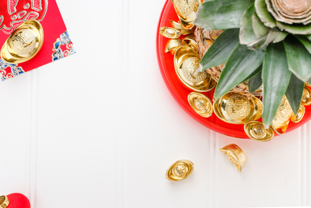 Chinese New year ang pow concept.Top view Pineapple with group of gold ingots in red tray on white wood table.on ingots mean wealthy.の写真素材