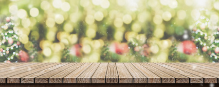 Empty brown wooden table top with abstract green blur christmas tree and snow fall background with bokeh light,Holiday backdrop,Mock up banner for display or montage of productの写真素材