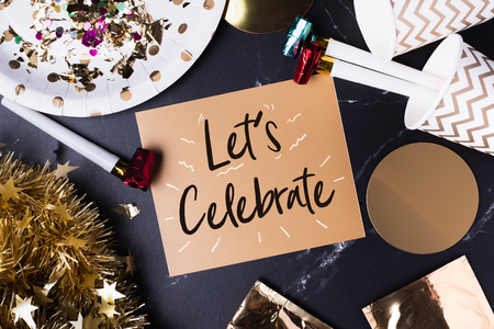 Letâs celebrate (handwriting) on golden greeting card with doodle line with party cup,party blower,tinsel,confetti.Holiday party time table top viewの写真素材
