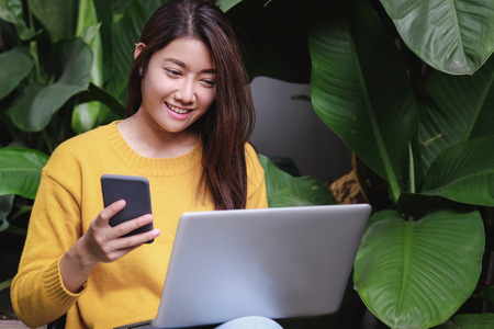 asian woman excited with sale promotion on website shop on laptop sitting on chair in garden at home.shopping online with credit card.Leisure digital lifestyleの写真素材