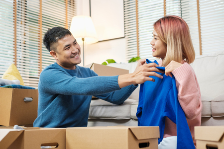Happy asian couple open cardboard boxes  while moving to new home at sofa in living room.unpacking for new houseの写真素材