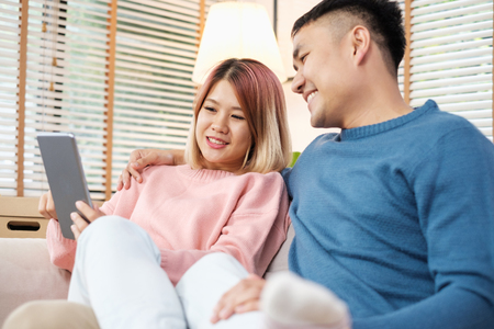 Asian couple watching video live on tablet on sofa in living room at home.lover spending time togetherの写真素材