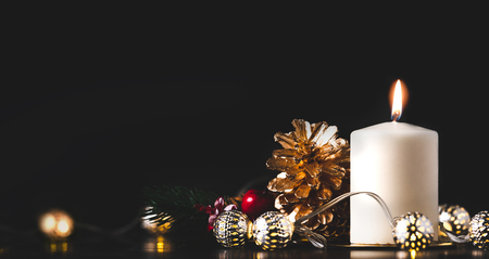Christmas white candle with golden pine cone,mistletoe and light string glowing on black marble table with dark background.holiday greeting card.Banner for display of design or contentの写真素材
