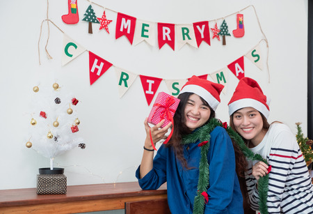 Asia girl friends wear santa hat in merry christmas and new year party exchange red gift box each other with smiling face,Xmas gift givingの写真素材