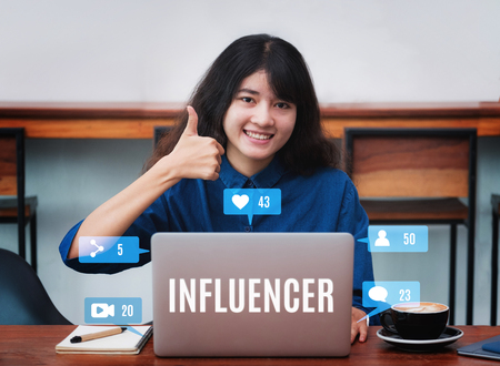 Asian woman influencer thumbs up and smile using laptop with coffee cup in cafe restaurant,woman blogger working outside office,digital lifestyle conceptの写真素材