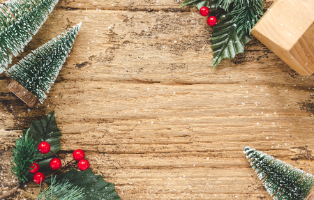 Top view of mini christmas tree and red burry leaf with wood home toy on rustic wooden table with snow fall.winter holiday seasonal greeting card.leave space to adding text or designの写真素材