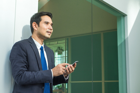 Businessman using mobile phone indise office building with smiling face after working hourの写真素材