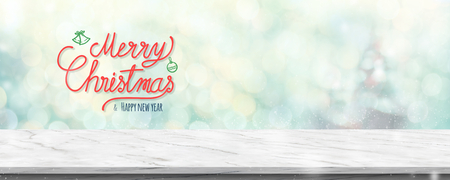 Red handwriting merry christmas and happy new year over white marble table with abstract blur green christmas tree and snow fall background with bokeh light.Mock up banner for display of productの写真素材