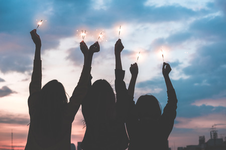 silhouette happy group of asia girl friends enjoy and play sparkler at rooftop party at evening sunset,Holiday celebration festive,teeage lifestyle,freedom and funの写真素材