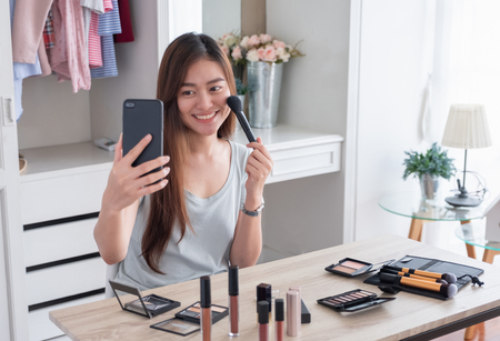 Asian young female blogger recording vlog video use mobile with makeup cosmetic at home online influencer on social media concept.live streaming viralの写真素材