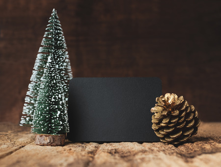Blank blackboard with christmas tree and gold pine cone and snow falling on grunge wood table and dark brown wooden wall.winter holiday greeting card mock up templateの写真素材