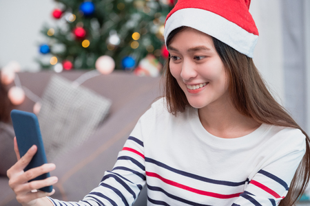 asia smile woman take selfie photo with mobile phone with blur christmas tree at xmas party,Live streaming video on social media event,Christmas holiday celebration partyの写真素材