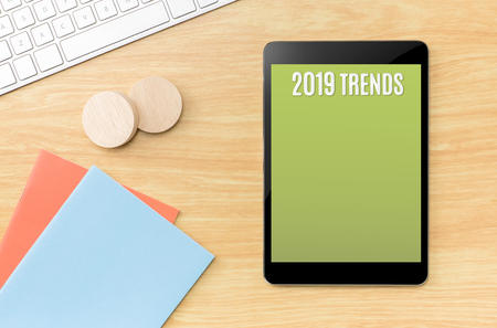 2019 trends on green screen tablet with blue notebook and keyboard on wooden table,new year resolutions.Mock up for display your contentの写真素材