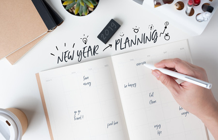 top view of hand writing  new year's planning on open calendar planner with doodle style for life resolution with modern office stationery and take away coffee cup on white desk in officeの写真素材