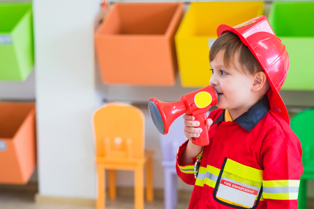 Caucasian boy kid dress up to fireman and use speaker at roll play classroom,Kindergarten preschool education conceptの写真素材