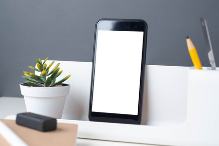 modern office stationery on white table and dark grey wall. mobile ,pencil, notepad,ruler,pen and pencil box with plant.Mock up mobile screen for display of design or contentの写真素材