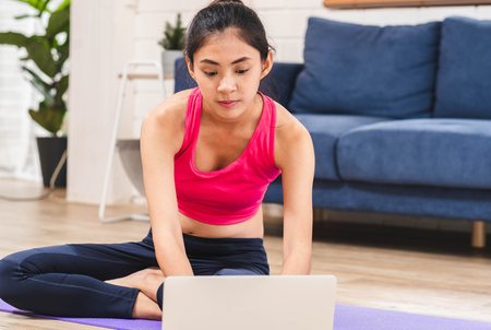 Asian woman searching video training onine on laptop and self training yoga pose in living room floor at home.Healthy lifestyle with technologyのイラスト素材