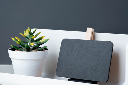 Black clip blackboard on modern pencil box and green plant in white pot on table and dark grey wall in office desk,mock up space for display of design or textの写真素材