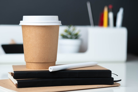 Coffee cup on notebook at modern office stationery on white table and dark grey wall.pencil,ruler,pen,pencil box and blackboard with plant.Mock up paper note for display of design or contentの写真素材