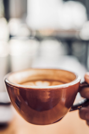 Close up hand holding a cup of hot cappuccino coffee cup with heart shape latte art blur cafe interior.food and drink concept.copy space for adding textの写真素材