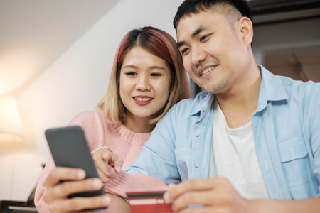 boyfriend hand holding mobile and credit card to shopping online for girlfriend on kitchen table in home.couple lifestyle conceptの写真素材