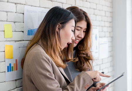 Two colleague businesswoman standing and discussion about work use tablet and drink coffee at office.Digital business lifestyle conceptの写真素材