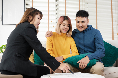 agent explain about house plan detail to asian couple at sofa in living roomの写真素材