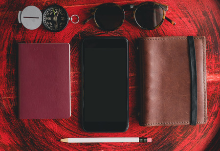 Set of mobile, passport ,notebook,sunglasses,compass and white pencil on rustic red wood round table near window.Tropical Summer Holiday vacation concept.clipping path on smartphone screenの写真素材