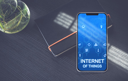 Internet of things (IoT) features icons on mobile phone screen lay on black notebook near window with sunlight on black wooden desk,Digital age technology conceptの写真素材