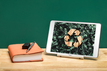 Recycle sign on green leaf on tablet app at office desk with book and pencil..enviroment eco system conceptの写真素材