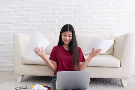 Asian woman freelancer stress emotion while working with laptop and paperwork at sofa in living room in house.work at home conceptの写真素材