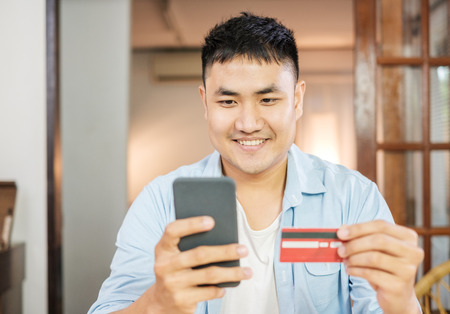 Asian man online shopping with credit card and mobile phone at home.digital lifestyle with technologyの写真素材