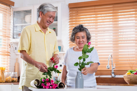 Asian Senior couple husband and wife flower arrangement to vase on table in kitchen at home in Valentine's Day.lovely senior couple conceptの写真素材