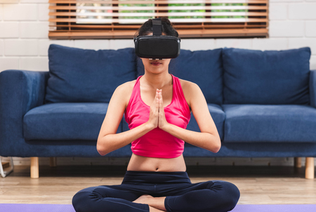 Asian woman use virtural reality glasses headset to training yoga pose online in living room floor at home.self learningの写真素材