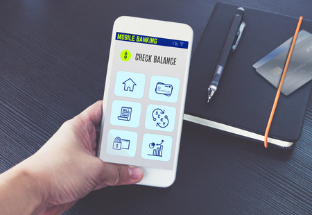 Hand holding mobile  banking app on screen with black notebook and credit card on black wooden desk,Digital banking technology conceptの写真素材