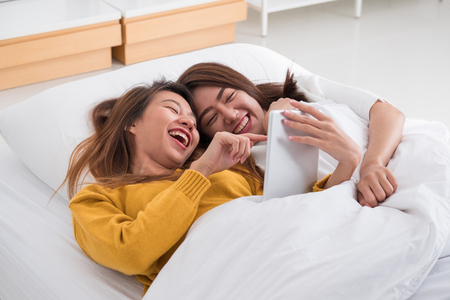 Asian lesbian lgbt couple lying on bed using tablet computer together in bedroom with happiness moment together,love wins conceptの写真素材