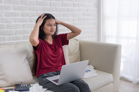 Asian woman freelancer stress emotion while working with laptop and paperwork at sofa in living room in house.work at home concept.の写真素材