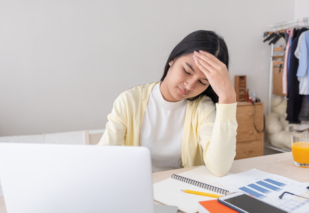 Asian female freelancer headache and stress while working with laptop on table in bedroom at home.Work at home concept.work from home conceptの写真素材