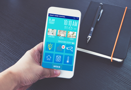 Hand holding mobile with home control app on black table when working.Smart home control with iot conceptの写真素材