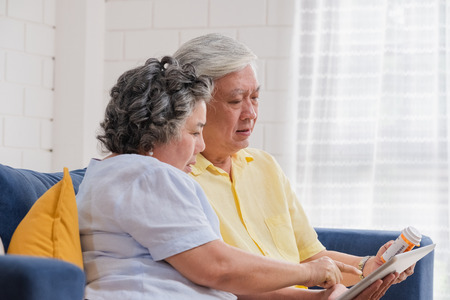 Asian senior couple use tablet searching prescription of pill while sitting on sofa at home,senior learn to use technology.aging at home.の写真素材
