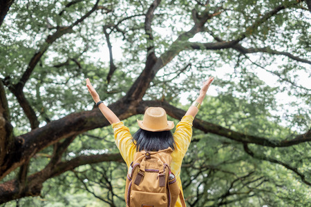 Asian traveler woman backpacker raise arm up  look at view and enjoy moment at green forest season,Freedom wanderlust travel.solo backpackの写真素材